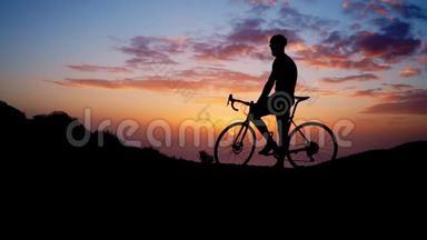年轻的运动员坐在山顶上的自行车上，戴着黄色的t恤头盔和<strong>运动器材</strong>，看着